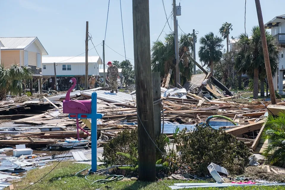 U.S. airmen in red berets and fatigues walk across rubble in Keaton Beach, Florida after Hurricane Helene heavily damaged the area.